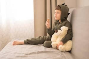 Child sitting on a couch with a teddy bear while staying home alone in a safe, calm environment