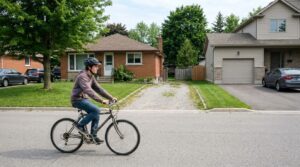 A teenage rider riding past the point where one suburban street becomes another, houses changing style.