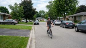 A teenage rider riding well out from the parked cars in a suburban street, holding a straight line.