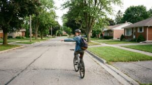 A teenage rider riding with the left arm held straight out to signal a turn, looking back at traffic behind.