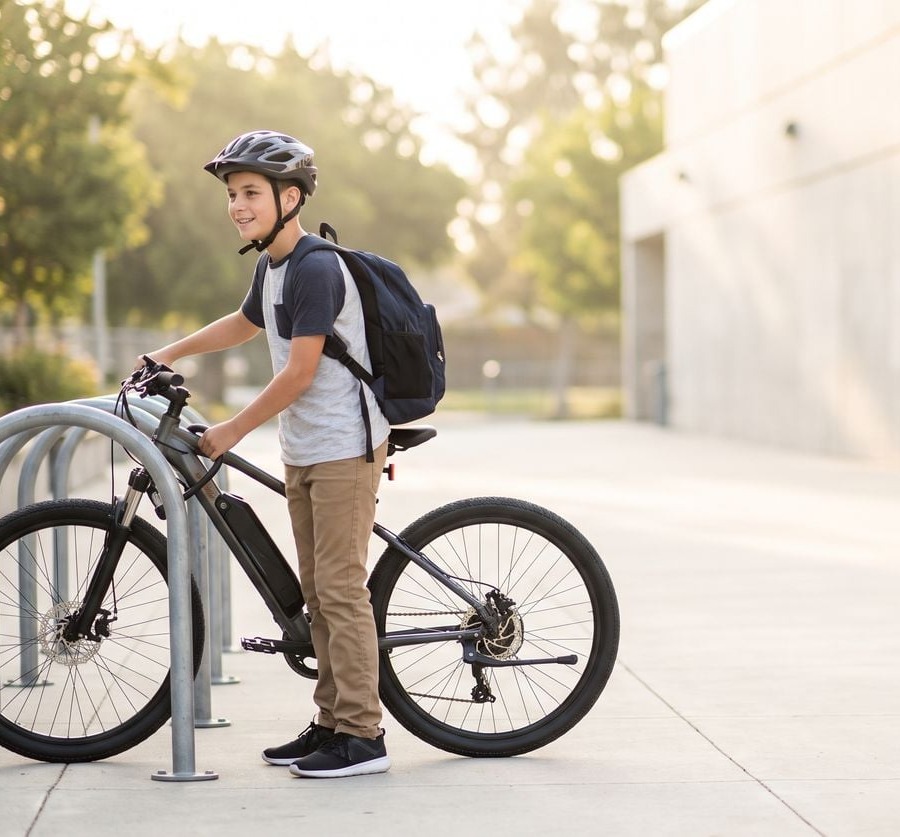 A boy in a helmet with his e-bike at the school rack