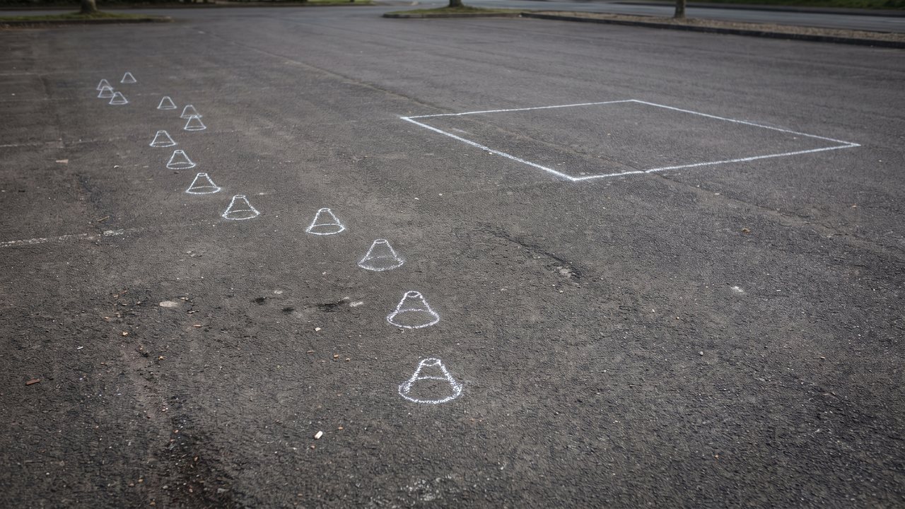 A line of six half tennis balls spaced evenly down a parking lot with a chalk rectangle drawn on the ground at the far end, and a machine waiting at the start.